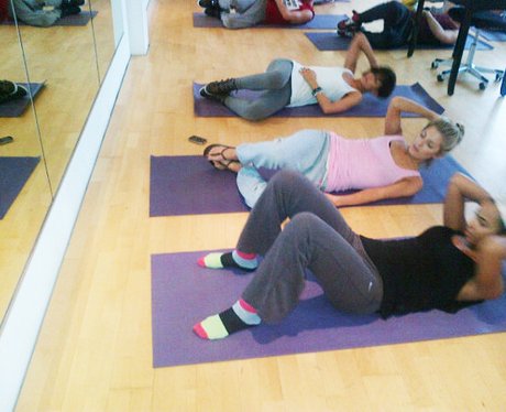 The Saturdays lie on gym mats and do sit ups