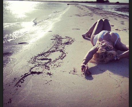 Rita Ora lying on a beach in a white swimsuit