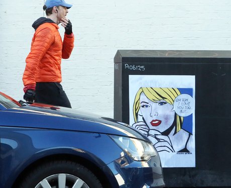 Tom Hiddleston walks past Taylor Swift poster